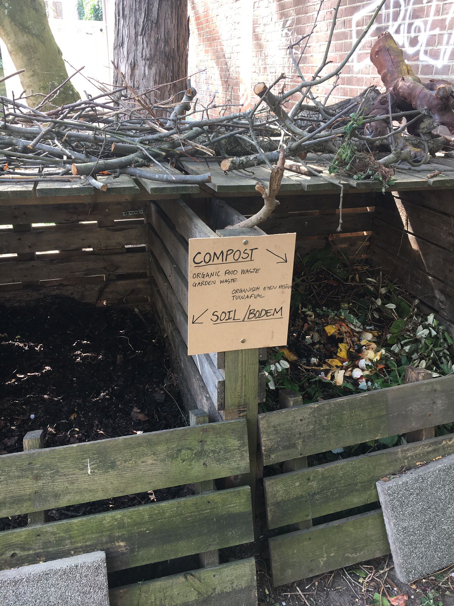Two-bayed compost bin, with green waste on the right and black compost on the left, in the center an instruction sign.